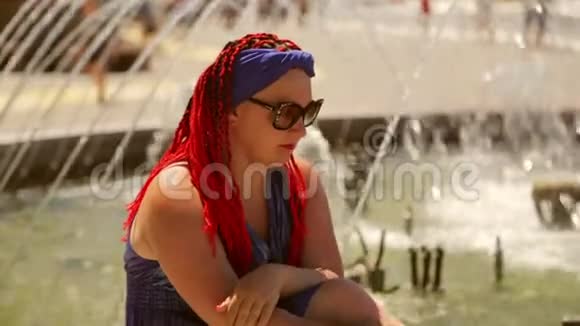 坐在喷泉边的一个忧郁的女人穿着蓝色的裙子梳着辫子视频的预览图
