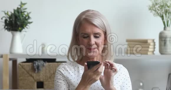 微笑的老太太在手机上激活虚拟数字语音助手视频的预览图
