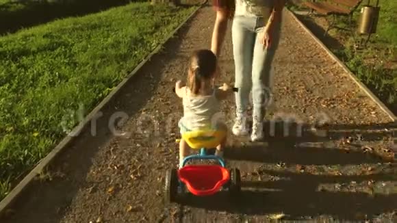 妈妈教女儿在公园里骑自行车幼儿学习骑自行车妈妈玩她的小东西视频的预览图
