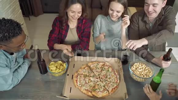 快乐的多民族朋友在家的客厅里喝啤酒吃披萨一起玩视频的预览图