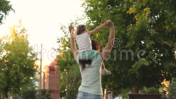 妈妈和女儿一起走在树下的肩膀上母亲扛着她心爱的孩子在公园里视频的预览图