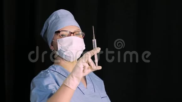 戴着医用口罩的女医生手里拿着一个黑色背景的注射器视频的预览图