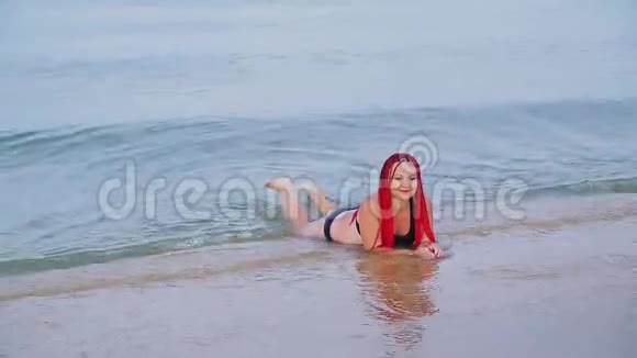 一个穿着红色辫子的黑色泳衣的犹太女人躺在海边的海水里视频的预览图