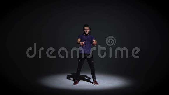男人穿着简单的灰色T恤和灰色牛仔裤在黑暗的背景上跳舞视频的预览图