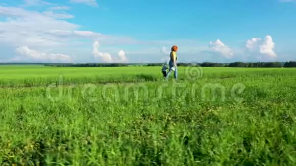 一个女人带着一个孩子走在路上沿着绿色的小麦地迎着一片白云的蓝天视频的预览图