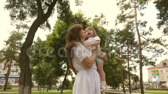 快乐的童年概念快乐的妈妈在户外公园拥抱小女儿漂亮的妈妈和她的宝宝在玩视频的预览图
