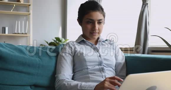 年轻的印度妇女在家坐在沙发上视频的预览图