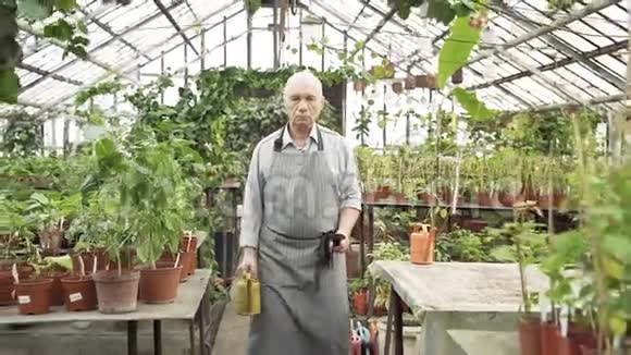一个围裙里带着工具和水壶的老人在温室里散步农业农业和园艺视频的预览图