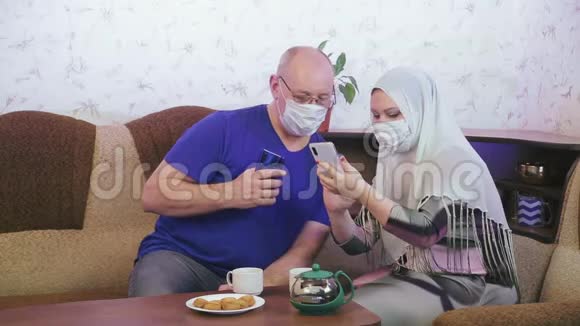 戴防护面具的穆斯林夫妇在家中的沙发上拍照预防冠状病毒视频的预览图