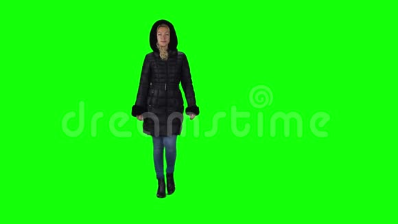 金发女孩穿着一件黑色的冬季外套头罩牛仔裤和靴子与绿色屏幕相衬慢动作视频的预览图