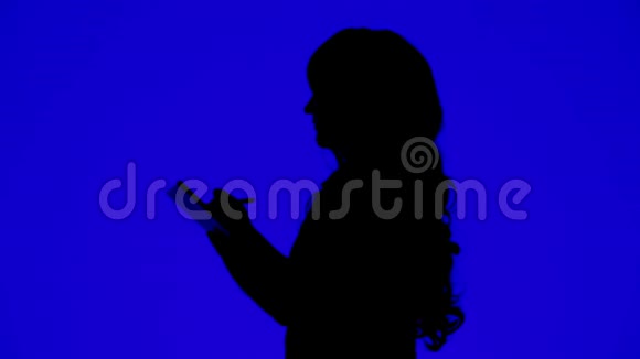 一个身材苗条卷发的女人用铅笔在蓝底笔记本上写字的剪影视频的预览图
