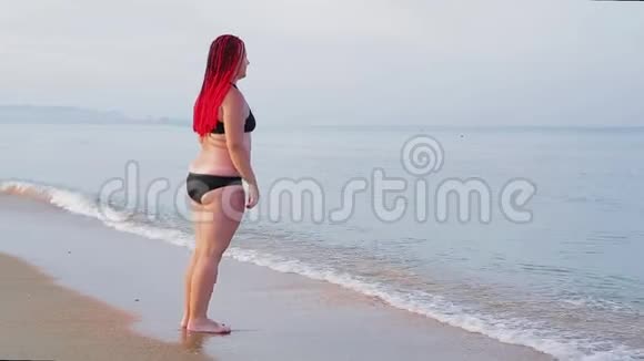 一个穿着红色辫子的黑色泳衣的女人从岸上的海里出来视频的预览图
