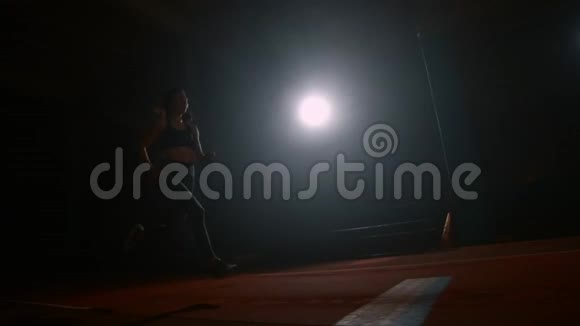 一名运动女子在体育场内奔跑在黑暗的背景下在体育场内缓慢地进行跳远运动视频的预览图