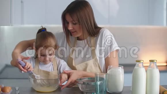 妈妈帮女儿学做饭一起穿着围裙在厨房里拍打和揉面为未来的馅饼和视频的预览图