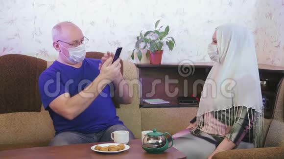 在家中沙发上拍摄的穆斯林夫妇戴着防护面罩进行检疫以预防冠状病毒视频的预览图