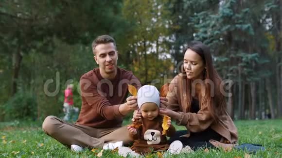 年轻的母亲父亲和小儿子在秋天的公园里玩树叶视频的预览图