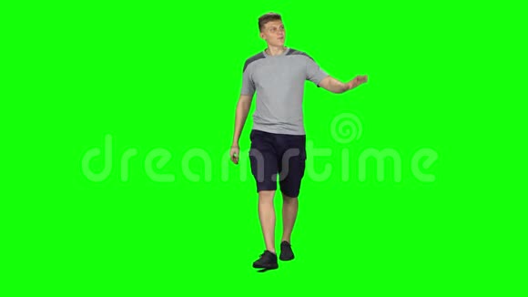 年轻人走着在绿色的屏幕上挥动他的手彩色钥匙视频的预览图