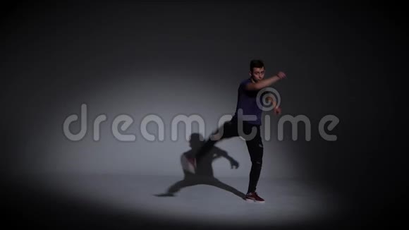 男人穿着简单的灰色T恤和灰色牛仔裤在黑暗的背景上跳舞视频的预览图