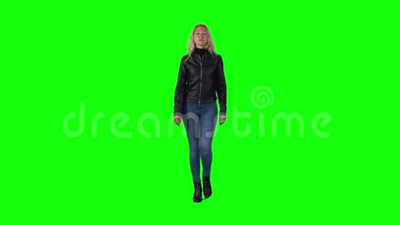 穿黑色皮夹克牛仔裤和靴子的金发女孩与绿色屏幕相映成趣慢动作视频的预览图