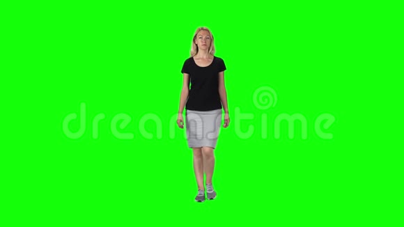 金发女孩穿着黑色T恤灰色裙子和运动鞋靠在绿色的屏幕上慢动作视频的预览图