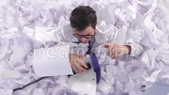 戴眼镜的恶毒男人办公室工作人员在一大堆皱巴巴的纸里哭泣视频的预览图