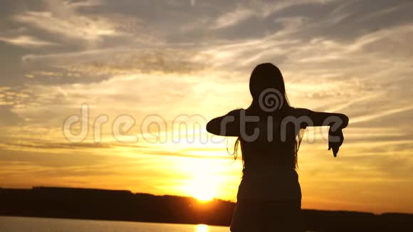自由开朗的女人留着长发的快乐女孩正在海滩上日落时跳舞笑着慢动作视频的预览图