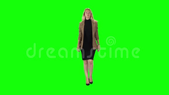 金发女孩穿着时尚的棕色夹克黑色连衣裙和高跟鞋穿着绿色的屏幕慢动作视频的预览图