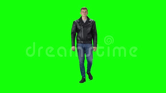 穿黑色皮夹克牛仔裤和运动鞋的年轻人穿着绿色背景慢动作视频的预览图