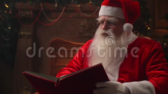 圣诞前夜圣诞老人在一种舒适的气氛中在壁炉和圣诞节的背景上读一本红色的书视频的预览图