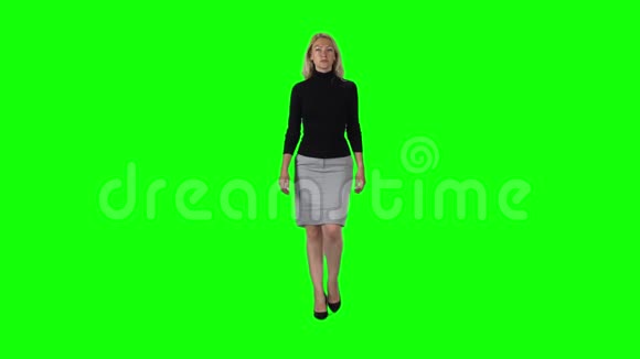 金发女孩穿黑色高领毛衣灰色裙子和高跟鞋与绿色屏幕慢动作视频的预览图