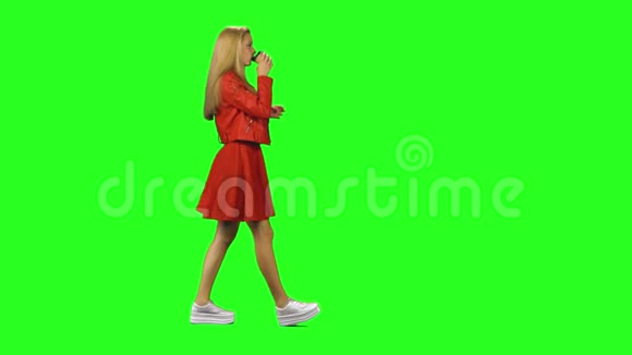 金发女孩平静地走着在绿色的屏幕背景上喝着咖啡铬钥匙4k射击侧写视图视频的预览图