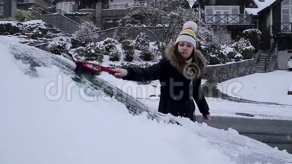年轻迷人的黑发女人在冬天用冰刮刀清理汽车上的积雪高清24FPS视频的预览图