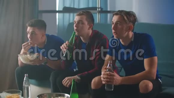 三个人坐在沙发上喝着啤酒看着电视一边跳着体育节目一边高兴地拥抱在一起视频的预览图