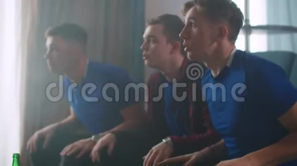 三个穿着蓝色T恤的男人看冰球比赛朋友们坐在沙发上欢呼鼓掌直视对方视频的预览图