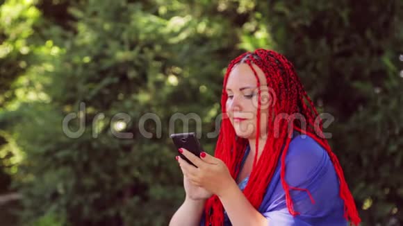 一个年轻的女人坐在公园的草地上在智能手机里的信使里交流视频的预览图