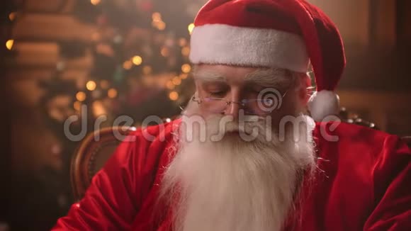 现代圣诞老人快乐的圣诞老人在手提电脑上工作坐在椅子上带着壁炉微笑视频的预览图