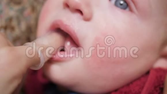 妈妈用戴在手指上的牙刷按摩器和口香糖凝胶按摩婴儿牙龈泰兴概念慢动作和特写视频的预览图