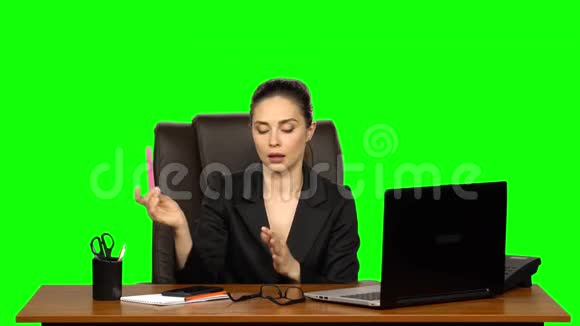 工作场所的女人正在用笔记本电脑工作在两部手机上说话锯钉子绿色屏幕视频的预览图