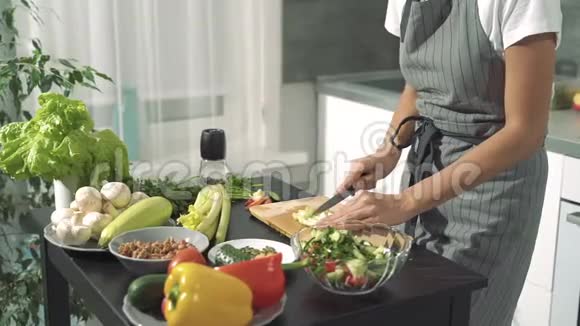 一个年轻女人的手在木板上剁碎新鲜芹菜做沙拉然后在碗里折叠到厨房里的其他蔬菜视频的预览图