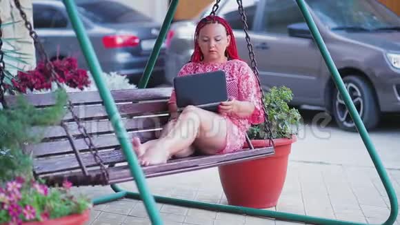 年轻的女性自由职业者正在家里院子里的秋千上用笔记本电脑工作视频的预览图