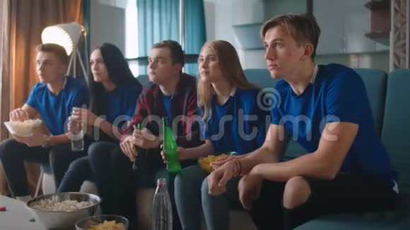 一群穿着蓝色t恤的朋友在电视上坐在沙发上带着爆米花和视频的预览图