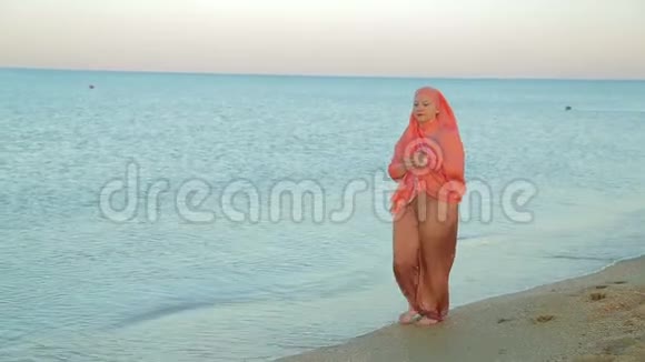 一位身穿橙色披肩的年轻穆斯林妇女沿着海滨散步视频的预览图