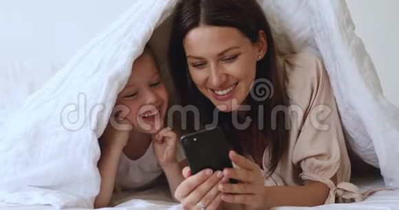 微笑的年轻母亲展示有趣的移动应用程序给快乐的女儿视频的预览图