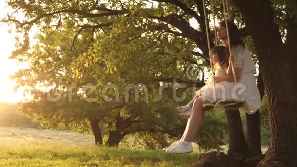 快乐妈妈在树上的公园里的秋千上摇动可爱的婴儿幸福家庭的概念梦想飞翔的概念视频的预览图