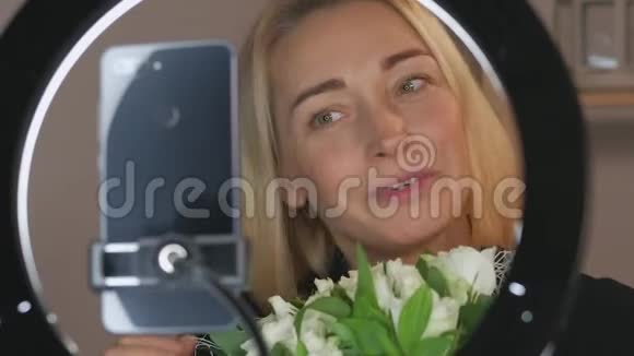 拥有一束鲜花的特写女博主用智能手机摄像头直播视频的预览图