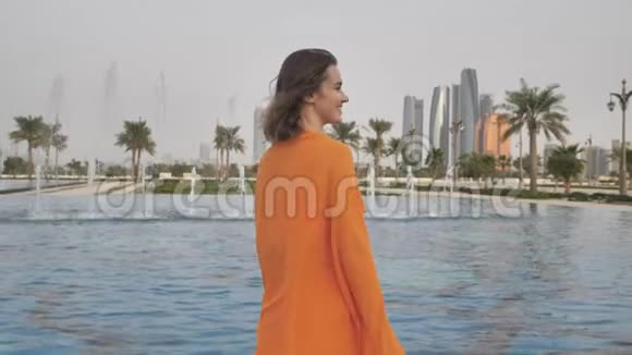 一个穿着橙色连衣裙的女孩走过傍晚的阿布扎比阿联酋视频的预览图