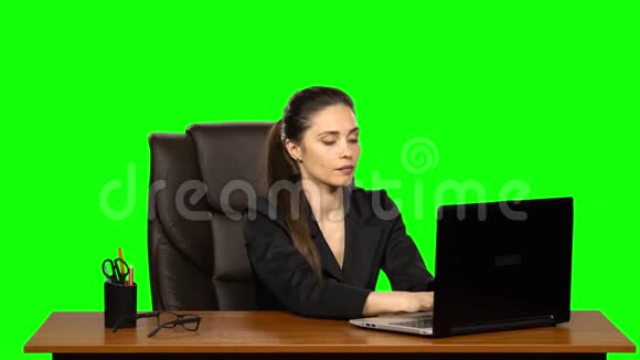 一位在笔记本电脑上工作的女商人一边看着摄像机一边开心地微笑着并展示ok标志绿色屏幕视频的预览图