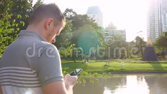 严肃的男人在公共公园用智能手机背景是摩天大楼视频的预览图