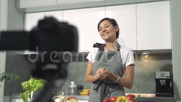 有魅力的年轻女性在家里的厨房里用数码相机录制了一段关于健康饮食的视频博客和社交媒体视频的预览图