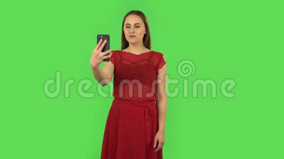 穿红色衣服的温柔女孩在手机上自拍然后看照片绿色屏幕视频的预览图